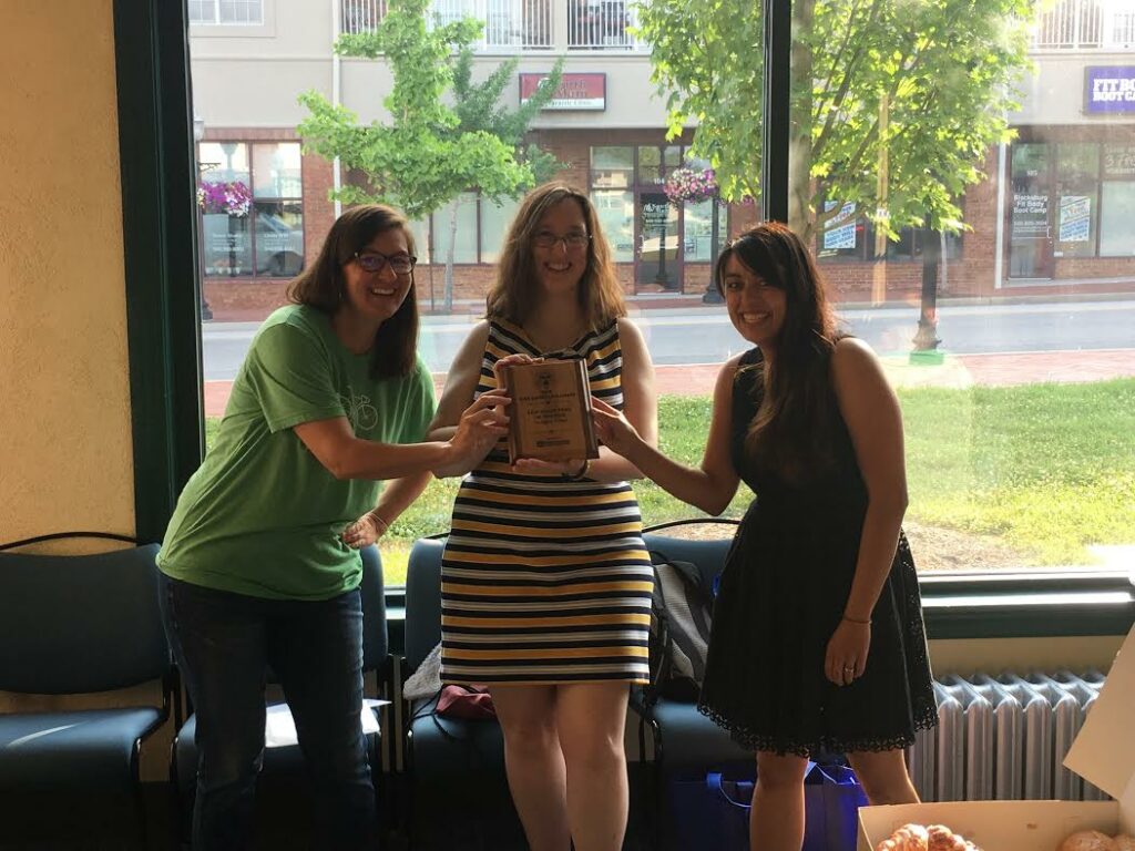 Three women pose with award plaque